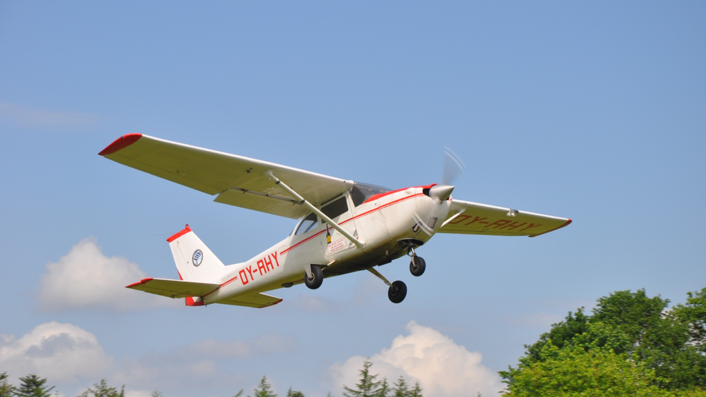 En Cessna 172 flyver over en græsbane, klar til at transportere faldskærmsspringere til deres springhøjde under en klar blå himmel.